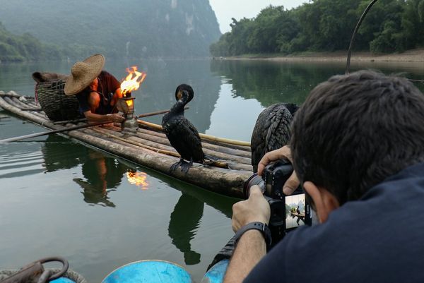A shot over Joel Santos's shoulder as he photographs a fisherman on his boat with his cormorant.