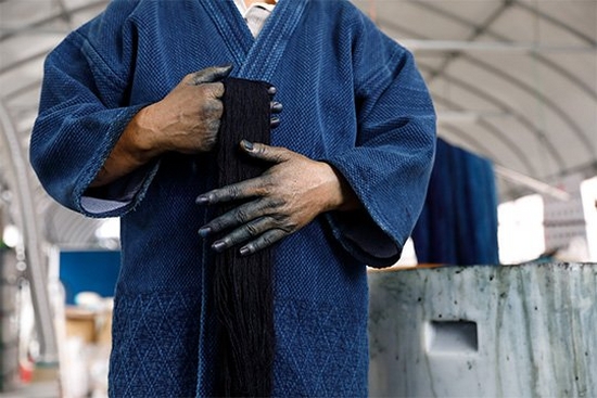 In a film still from Made in Japan, a denim factory worker holds a piece of fabric with indigo-stained hands.