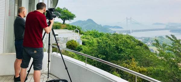 Made in Japan filmmakers Jack Flynn and Nick David stand on a balcony filming a distant bridge.