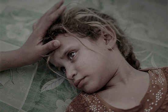 A blonde five-year-old girl lies on a green printed mattress, a hand stroking her hair