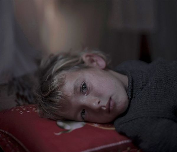 A blonde child lies with her head on a red pillow, looking at the camera