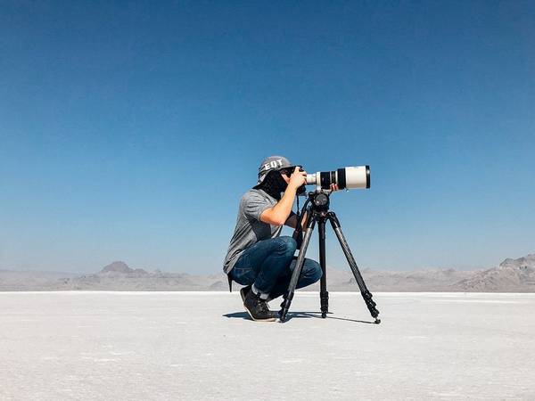 Photographing a cycling world record: Matt Ben Stone crouches behind his Canon camera and lens on a tripod in Utah salt flats.