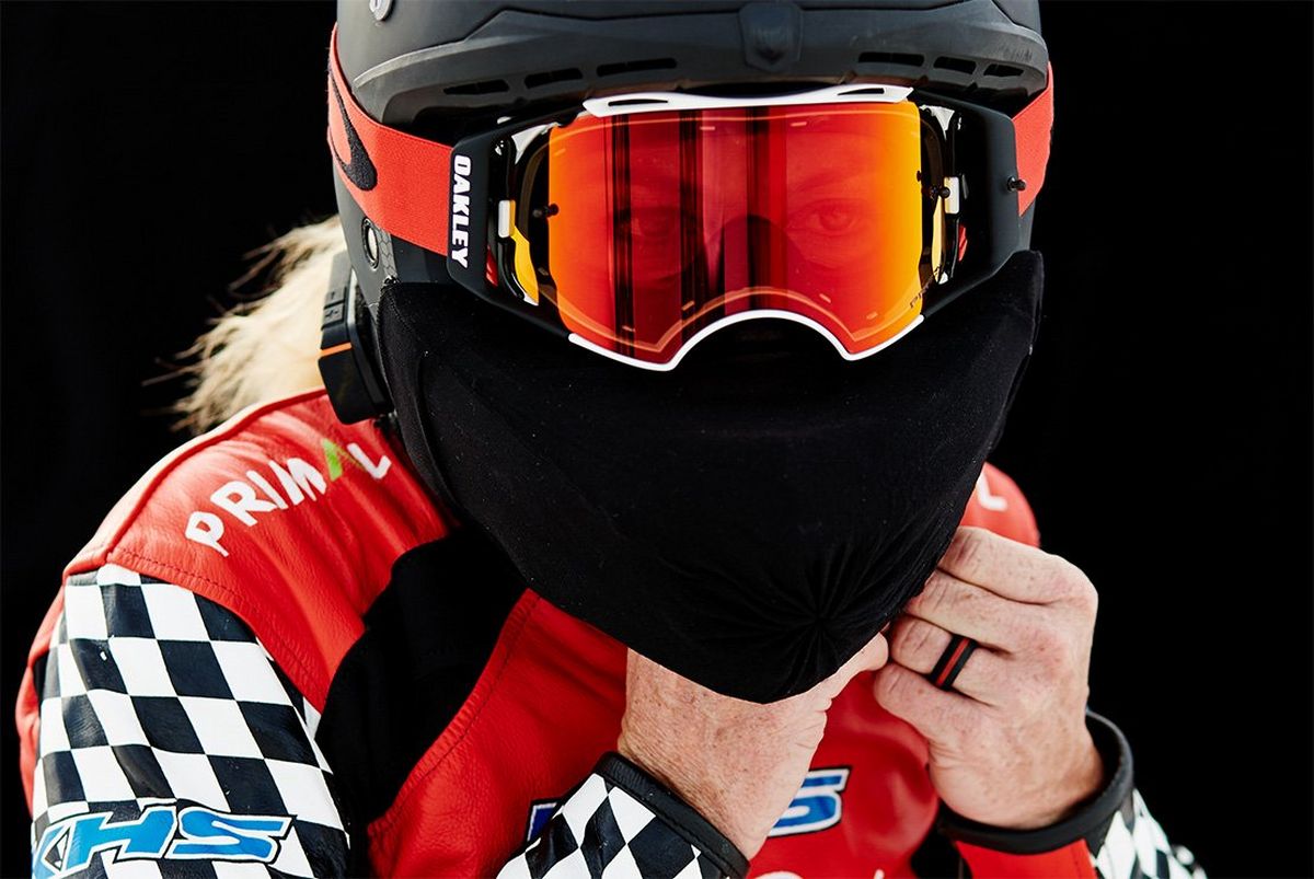 A woman fastens a face-covering black helmet and goggles.