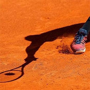A tennis player's shadow is seen on a red clay court.