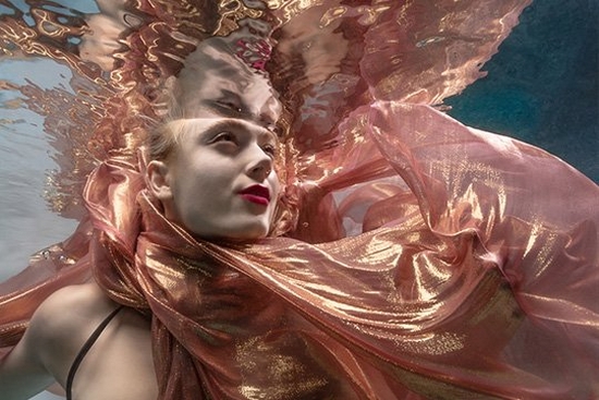 A woman submerged in water with a pink and gold scarf billowing around her.