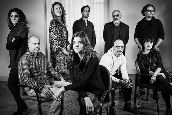 Nine men and women stand or sit in a group, in a room set up with photographers' light stands. The black and white photo shows Mashid Mohadjerin, Ilvy Njiokiktjien, Daniel Etter, Roberto Koch, Paolo Pellegrin, Alvaro Ybarra Zavala, Carolina Arantes, Magnus Wennman, Simona Ghizzoni.