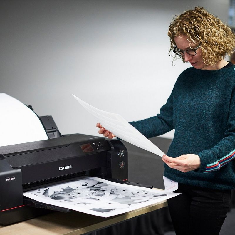 Helen Bartlett stands next to a Canon imagePROGRAF PRO-1000 printer looking at an A2 black and white photo print.