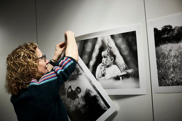 Helen Bartlett securing her monochrome A2 prints of children and families to the wall.