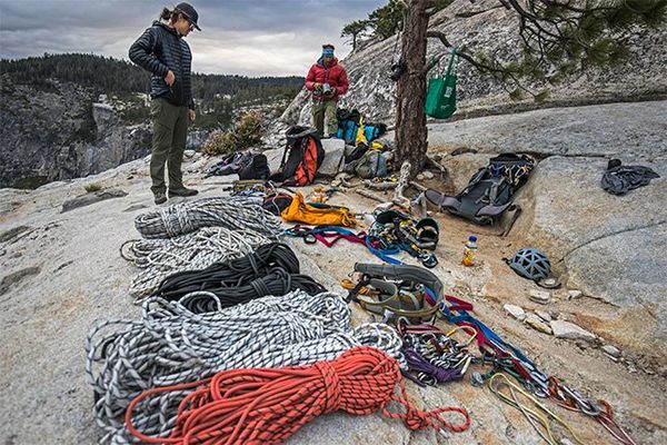 Ropes and climbing equipment laid out over a rocky clearing as two of the crew pack up after filming.