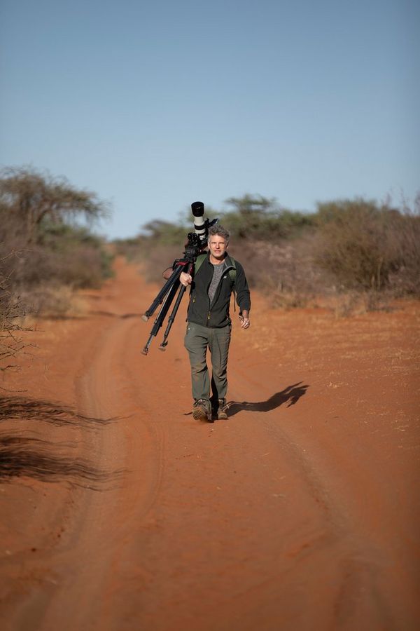 Camera operator Bosie Vincent carrying a Canon EOS-1D X Mark III, attached to a tripod, down a desert road.