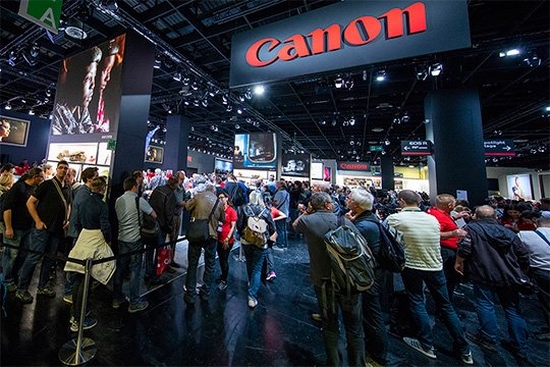 In the Canon area at photokina, visitors walk down an area lined with gallery images, a Canon logo above them.