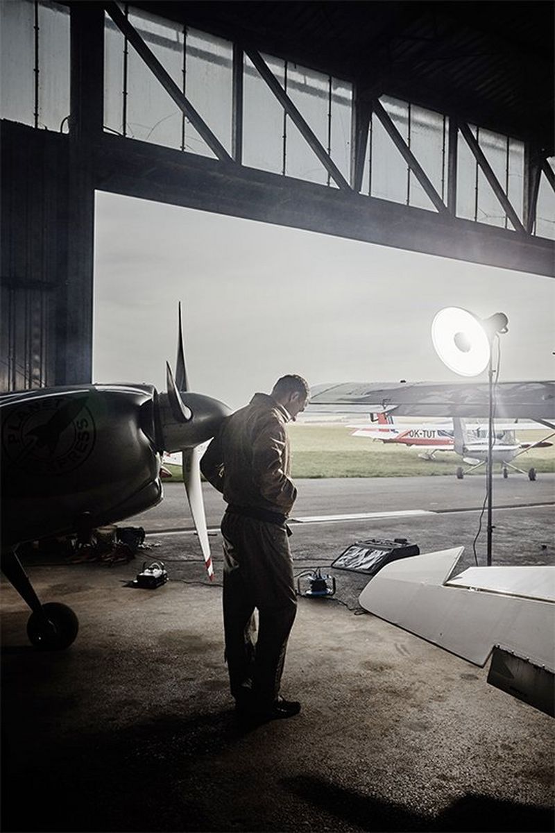 Martin Šonka stands in an aircraft hangar beside a small plane. Portrait by David Turecký on a Canon EOS 6D.
