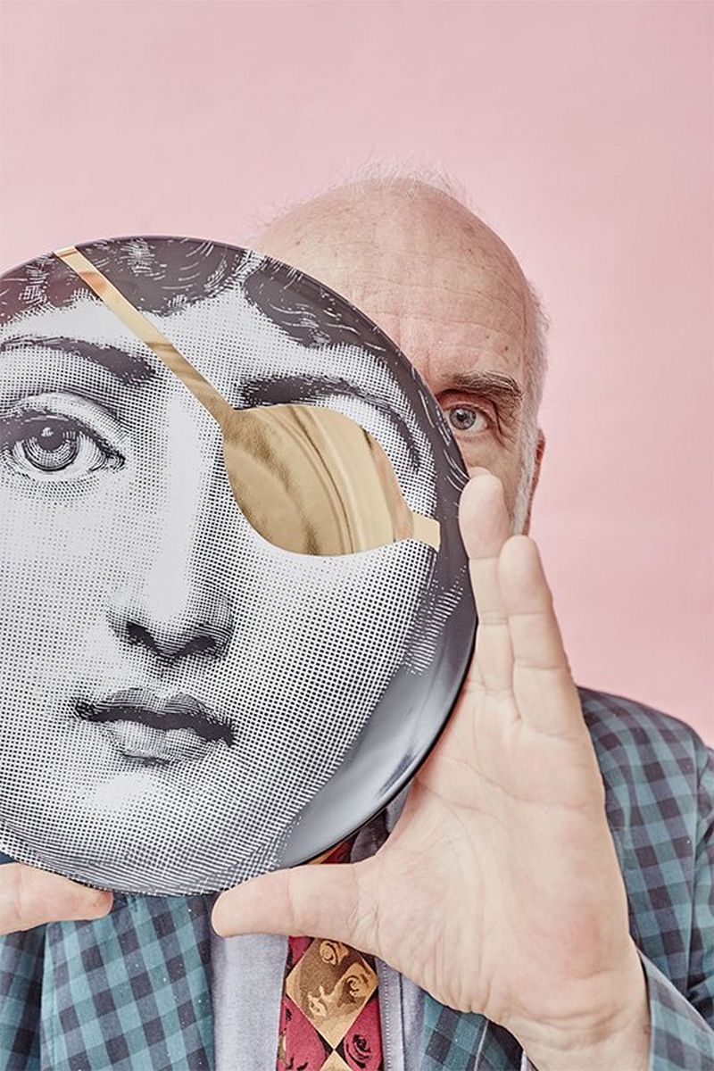 Designer Barnaba Fornasetti holds a mask with a single, large eye hole in front of his face. Colourful portrait by David Turecký on a Canon EOS 6D.