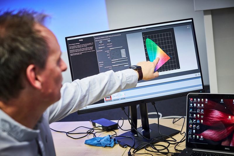 A man points to a monitor with a colour profile chart on the screen. 