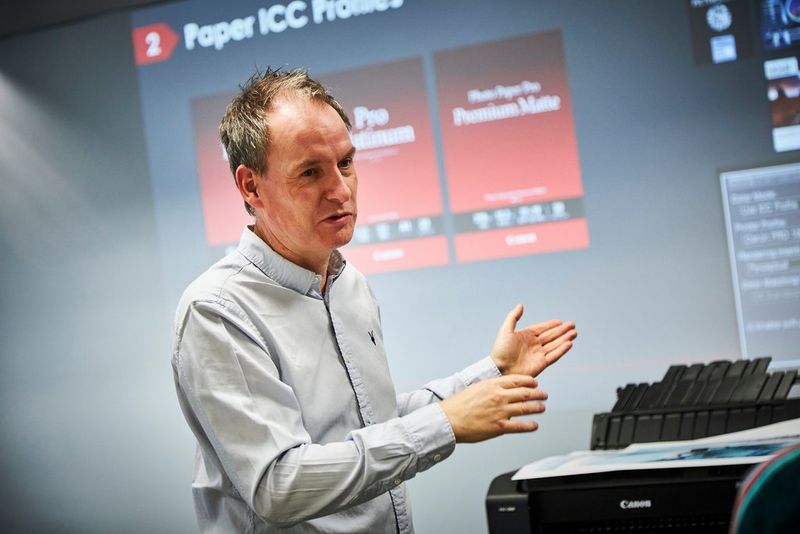 A man stands in front of a screen giving a presentation on printing.