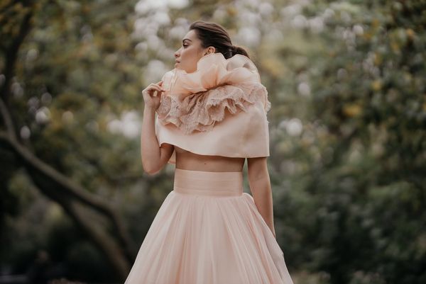 A model in a frilly wedding dress, photographed against a blurred background of tangled greenery.