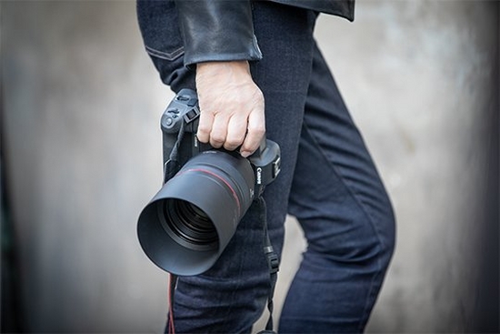 A photographer holds a Canon ֽ_격- with an RF 85mm F1.2L USM lens.