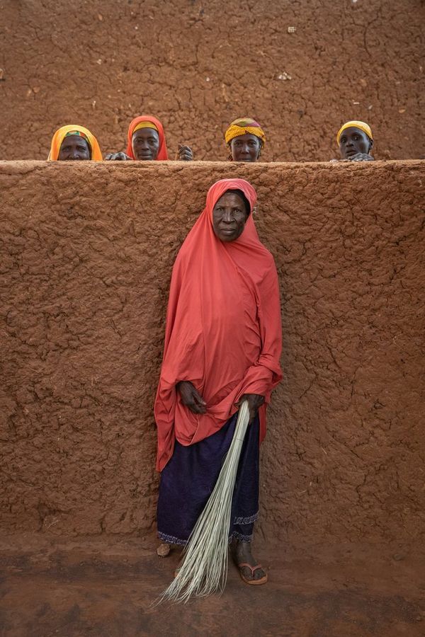 A woman stands with her back to a wall in Niger; four other women stand behind the wall, with just their heads visible. Taken by Joel Santos.