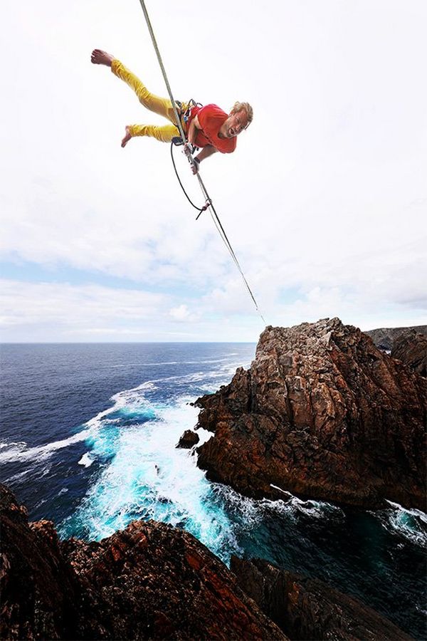 A slackliner balances on his hands on a rope over the sea, shot from below.