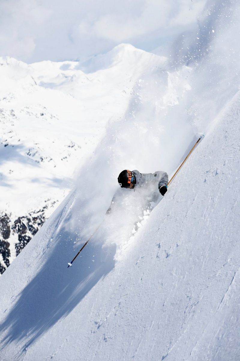 A skier seems to be engulfed in snow as he skis down a 45-degree slope, one of his stocks in front and one trailing behind.