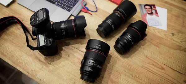 A Canon DSLR with a Canon EF 24-70mm f/4L IS USM lens on a desk alongside three other Canon lenses.