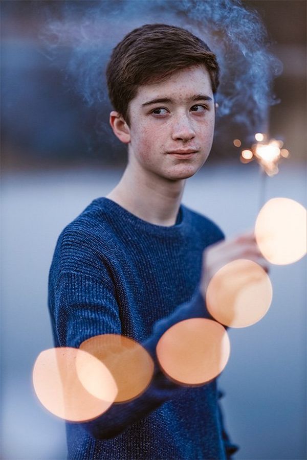 A boy holds a sparkler. Golden circles of light appear in front of him. Photo by Rosie Hardy with a Canon RF 85mm F1.2L USM lens.