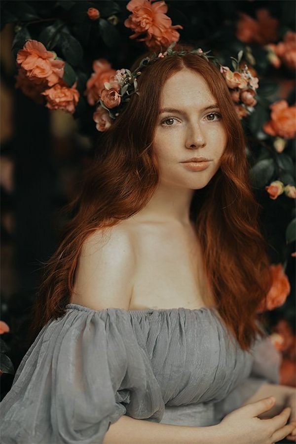 A brunette woman in a chiffon top sits by a pink camellia bush. Photo by Rosie Hardy with a Canon RF 85mm F1.2L USM lens.