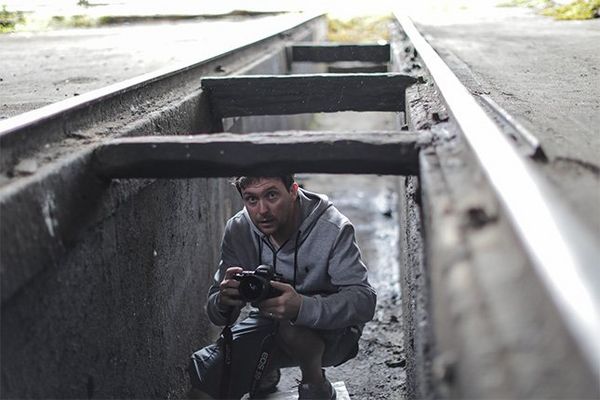 Photographer Samo Vidic crouches in the cavity underneath a train garage rail rack, holding his Canon ֽ_격-.