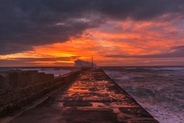 Sunset over the sea wall at Porthleven, Cornwall, streaking the sky with red and gold. Photo by Carla Regler.