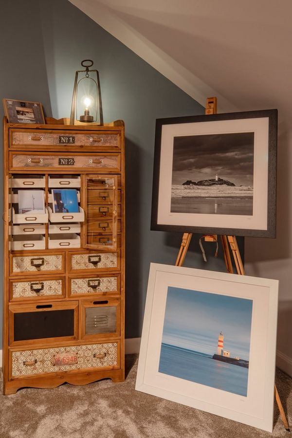 Photo prints displayed on an easel next to an ornate wooden chest of drawers, with smaller prints in some of the drawers.