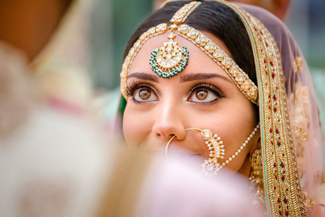 An Indian bride, photographed over her groom's shoulder, looking up at him.