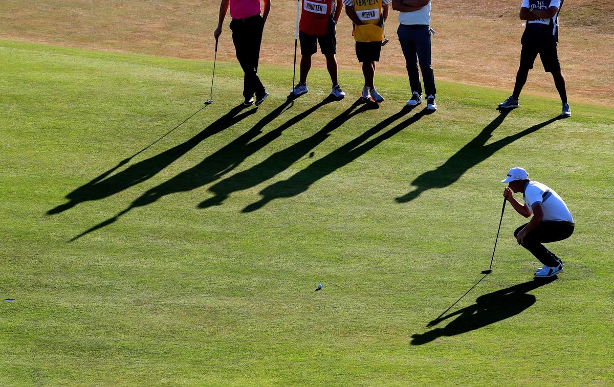 A golfer squats on his knees to line up a shot on the green, as five others watch. Taken by Marc Aspland.