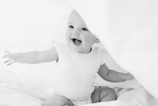 A toddler sits laughing happily under a sheet. Taken by Helen Bartlett.
