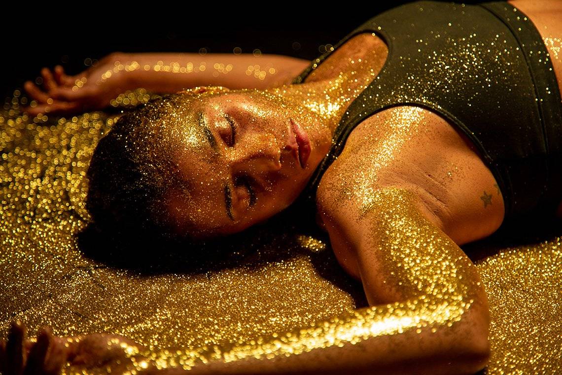 In a still from Perrault Pictures' film Return of the Golden Girl, kickboxer Jemyma Betrian lies in a boxing ring unconscious, covered in gold glitter. 