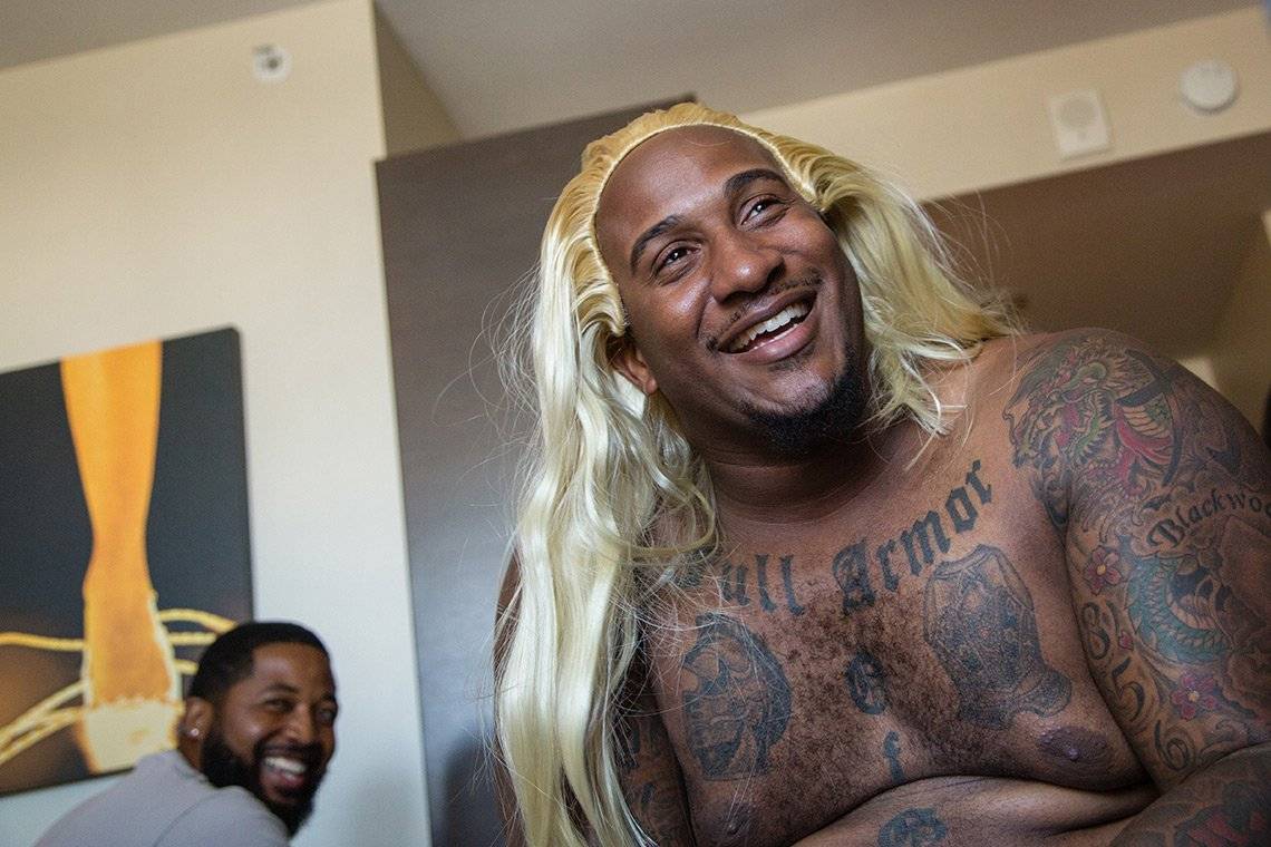 Portrait of American football player Mike Daniels topless, wearing a long blonde wig and laughing.