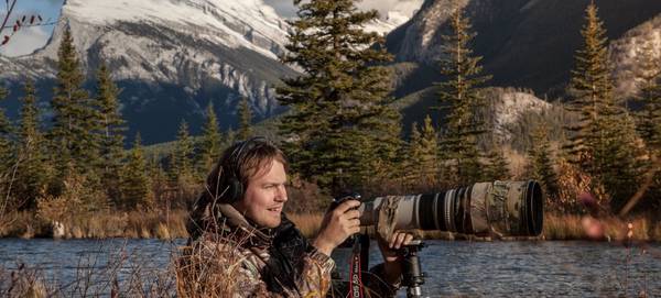 Vladimir Medvedev shooting with a Canon camera and lens by a stream with mountains in the background. ? Vladimir Medvedev