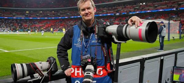 Photographer Tom Jenkins stands by the side of a football pitch with three Canon cameras fitted with telephoto lenses.