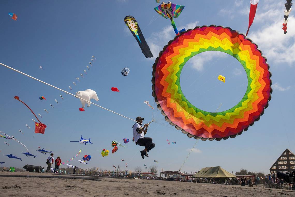 A kite-handler is lifted off the ground by his circular, rainbow-coloured kite. Photo by Ulla Lohmann.