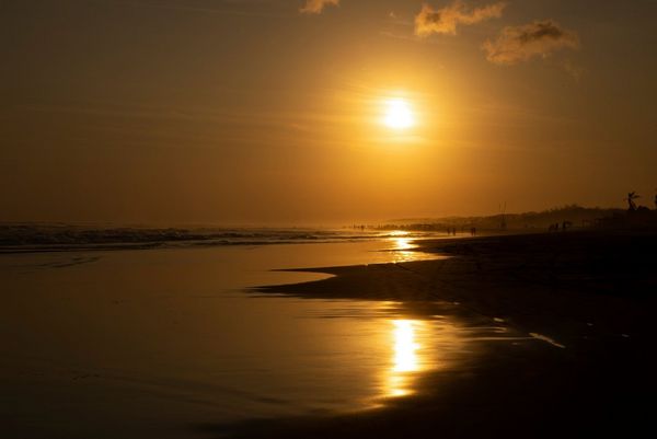 The setting sun is reflected in the water at the seashore.