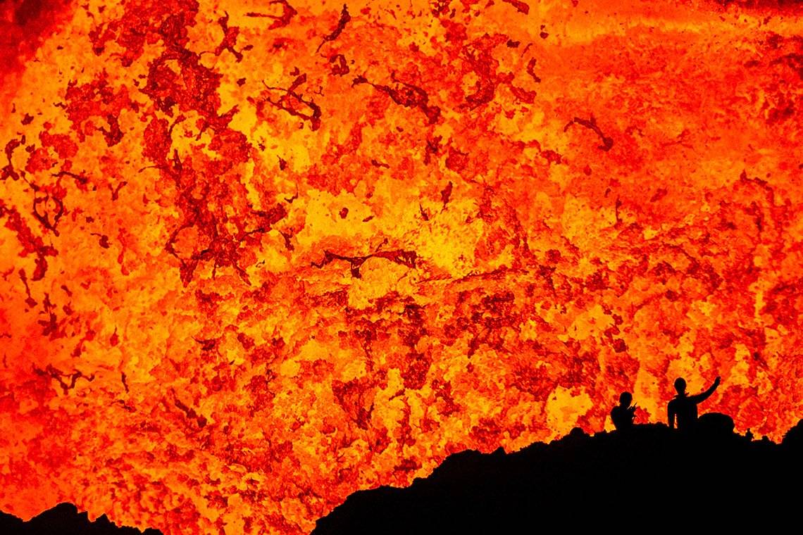 Two scientists silhouetted against the lava lake inside the Benbow crater on the volcanic island of Ambrym. 