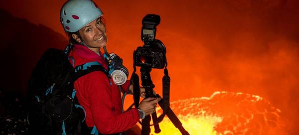Canon Ambassador Ulla Lohmann standing at the edge of a lava-filled crater, holding a Canon camera attached to a tripod.