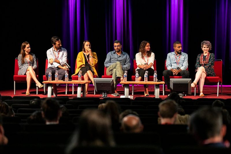A panel sit on a stage in discussion, beneath a picture of girls in hijabs holding Canon cameras.