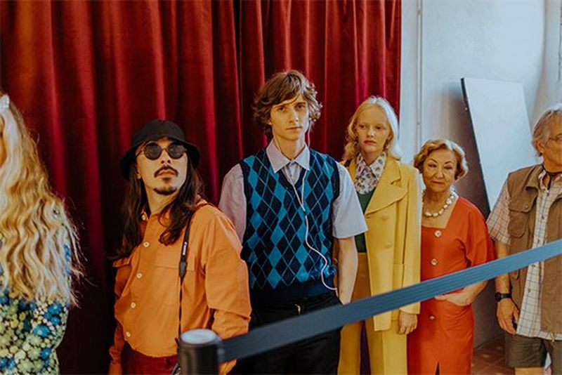 People in vintage clothing stand in a line as if waiting to enter somewhere.