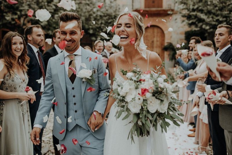 A bride and groom walking hand-in-hand between two rows of people, with confetti in the air.