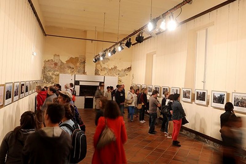People walk around an exhibition room looking at the printed photographs on the walls.