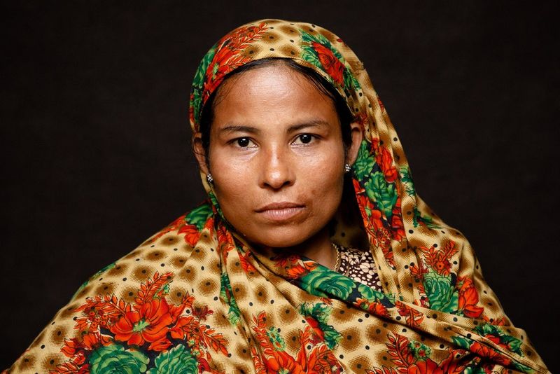 A woman with short, dyed red hair and tattoos wears a lilac top.