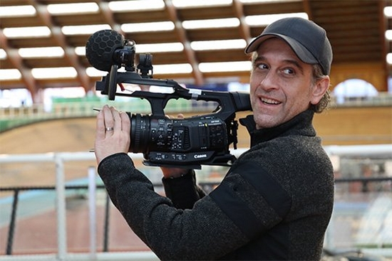 Filmmaker Sbastien Devaud holds a Canon XF705 camcorder to film, and smiles.