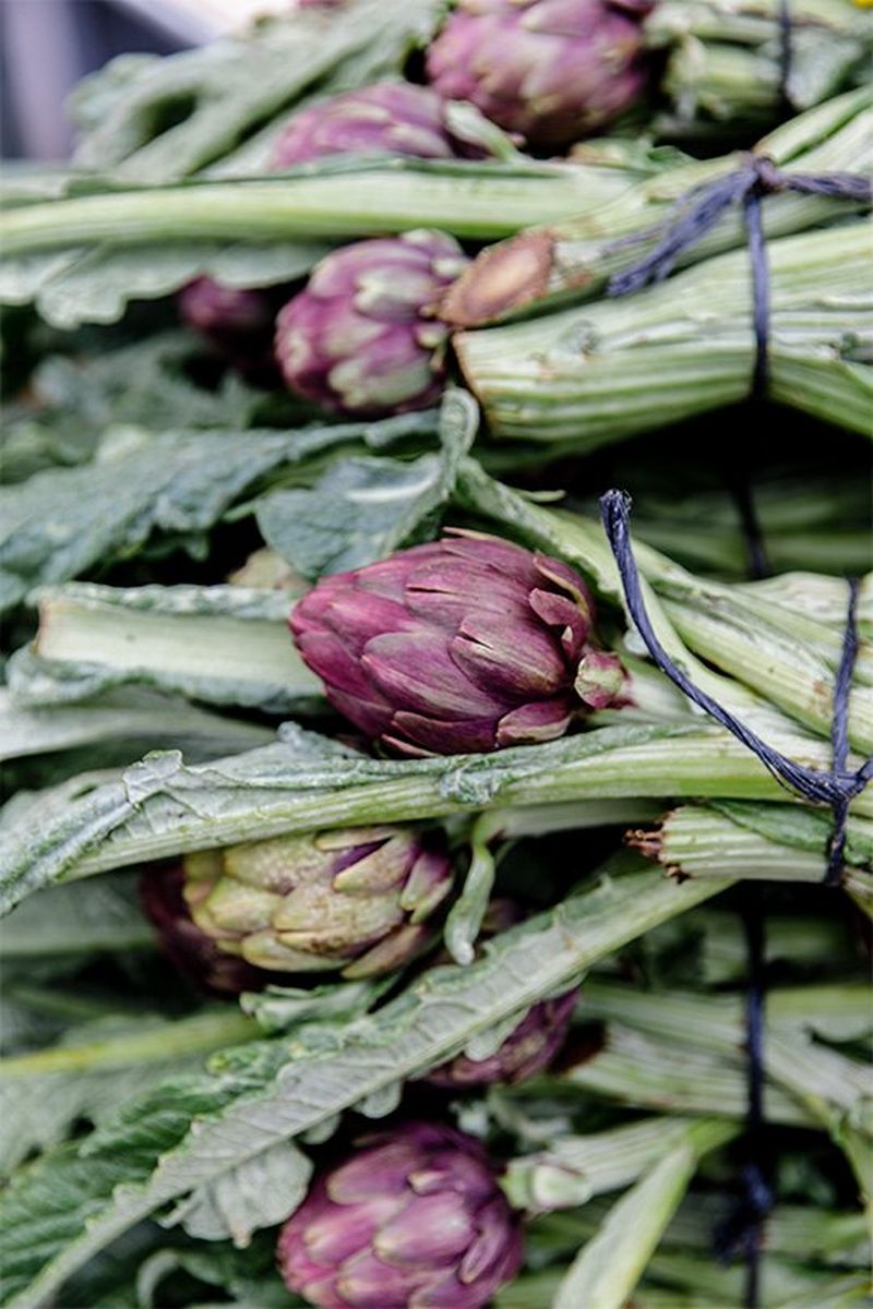 Artichokes in bundles are stacked up at a market. Photo by Annapurna Mellor with a Canon EF 24-70mm f/2.8L II USM lens.