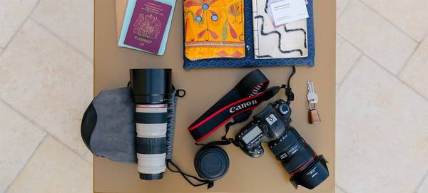On a table sits a Canon DSLR, two Canon lenses, a passport and travel diary.
