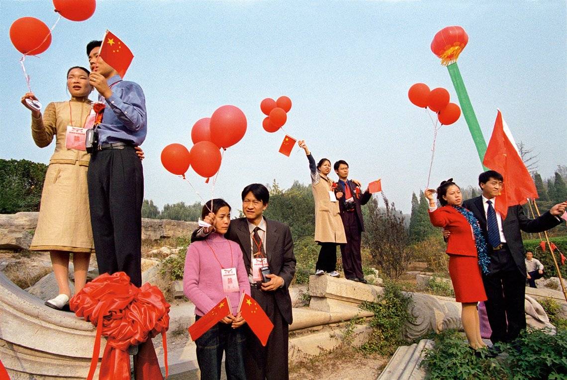 A wide shot of four couples holding red balloons, standing in the remains of an ancient palace. 